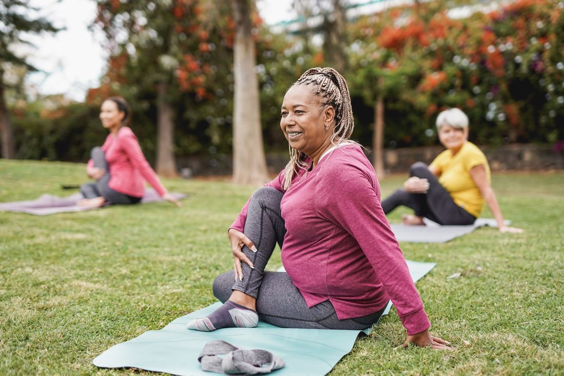 Three people stretching on yoga mats in a park.